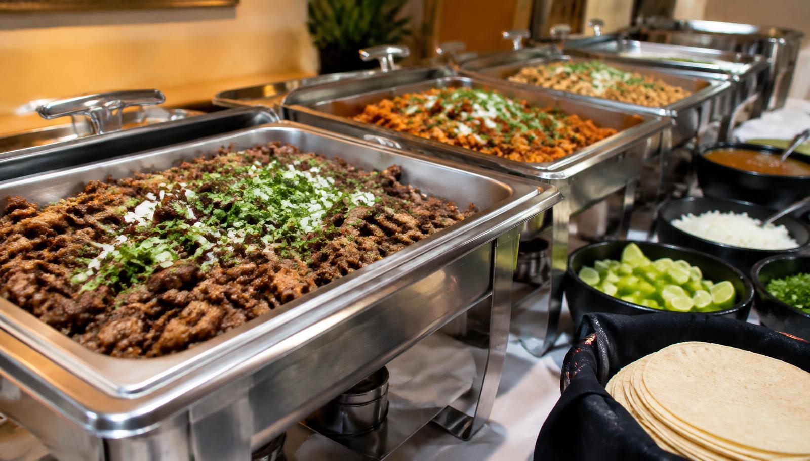 Línea de buffet con carnes y guarniciones en recipientes calientes